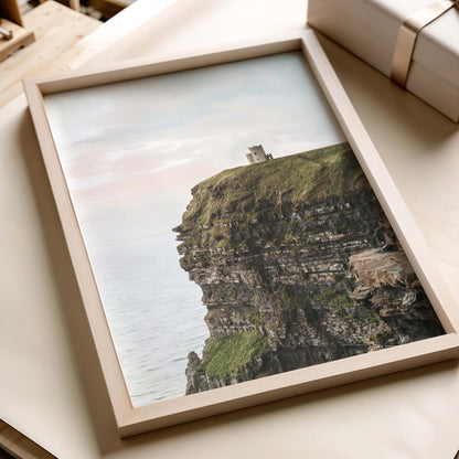 Close-up of framed photograph showing rocky Irish coastal cliffs, ocean and a distant structure, in white and grey tones