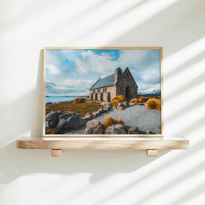 Framed Church of the Good Shepherd Lake Tekapo photography print in natural wood frame on minimalist wooden shelf against white wall with dappled shadows