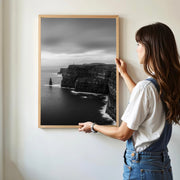 Woman hanging framed black and white print of the Cliffs of Moher in minimalist room