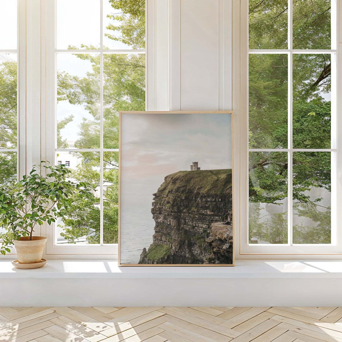 Framed Cliffs of Moher print in a bright room with tall windows, potted plant and wooden floor, beige and green tones