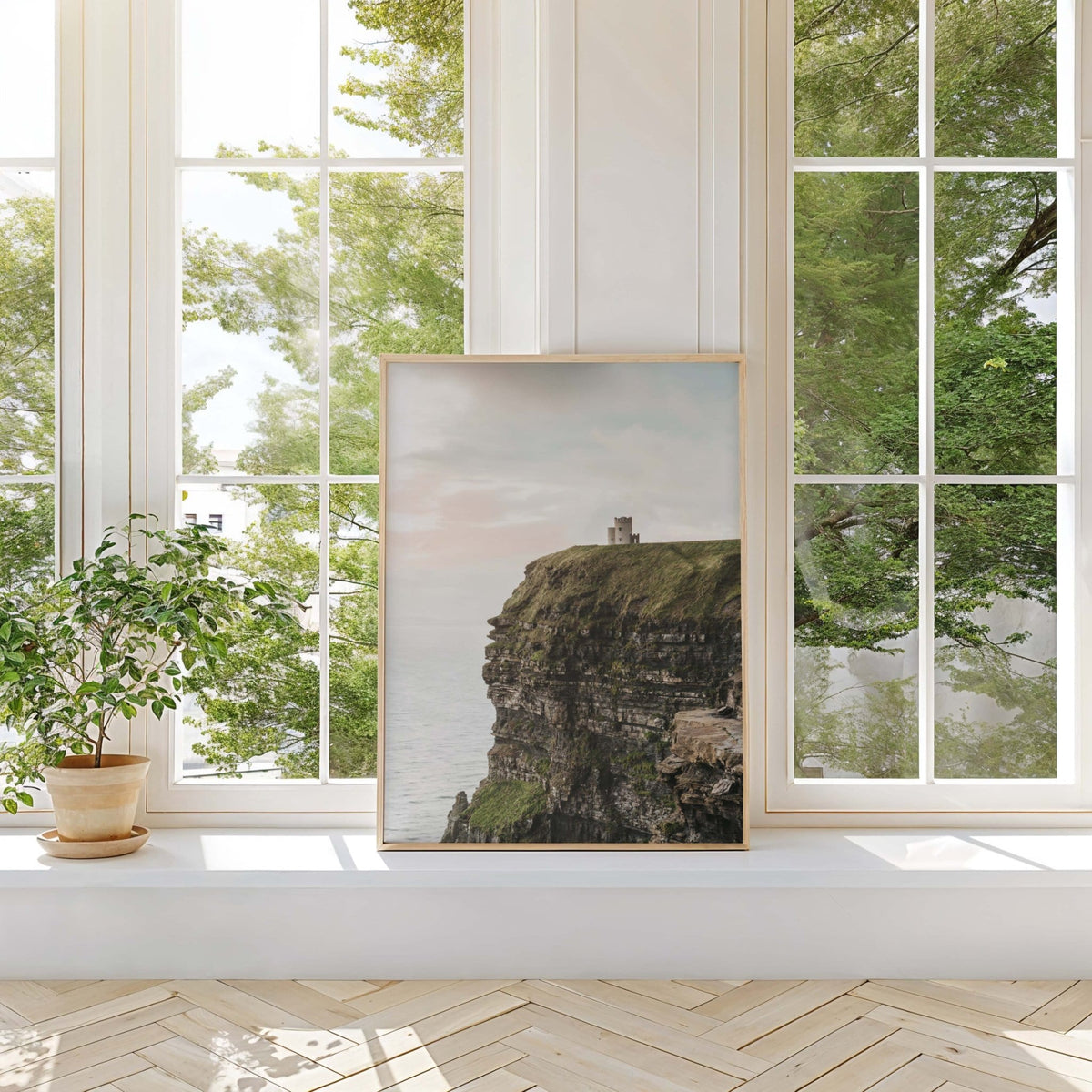 Framed Cliffs of Moher print in a bright room with tall windows, potted plant and wooden floor, beige and green tones