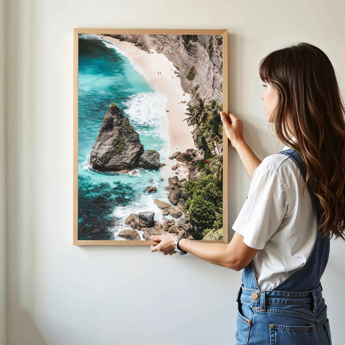 Woman hanging Diamond Beach Nusa Penida aerial framed wall art print in natural oak wood frame on white wall