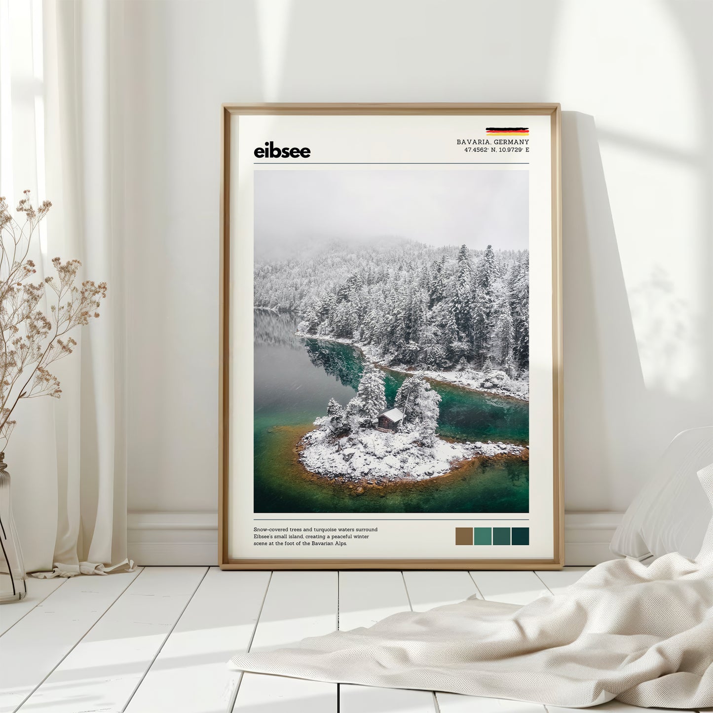 Natural wood framed Eibsee winter island cabin Bavaria Germany print leaning against white wall on white floorboards in minimal Scandinavian interior