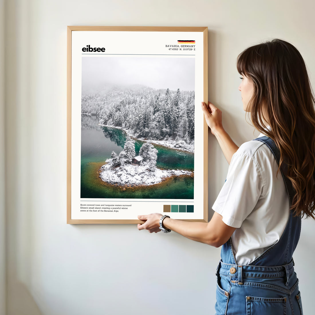 Woman hanging framed Eibsee winter island cabin Bavaria Germany photography print in natural oak frame on white wall