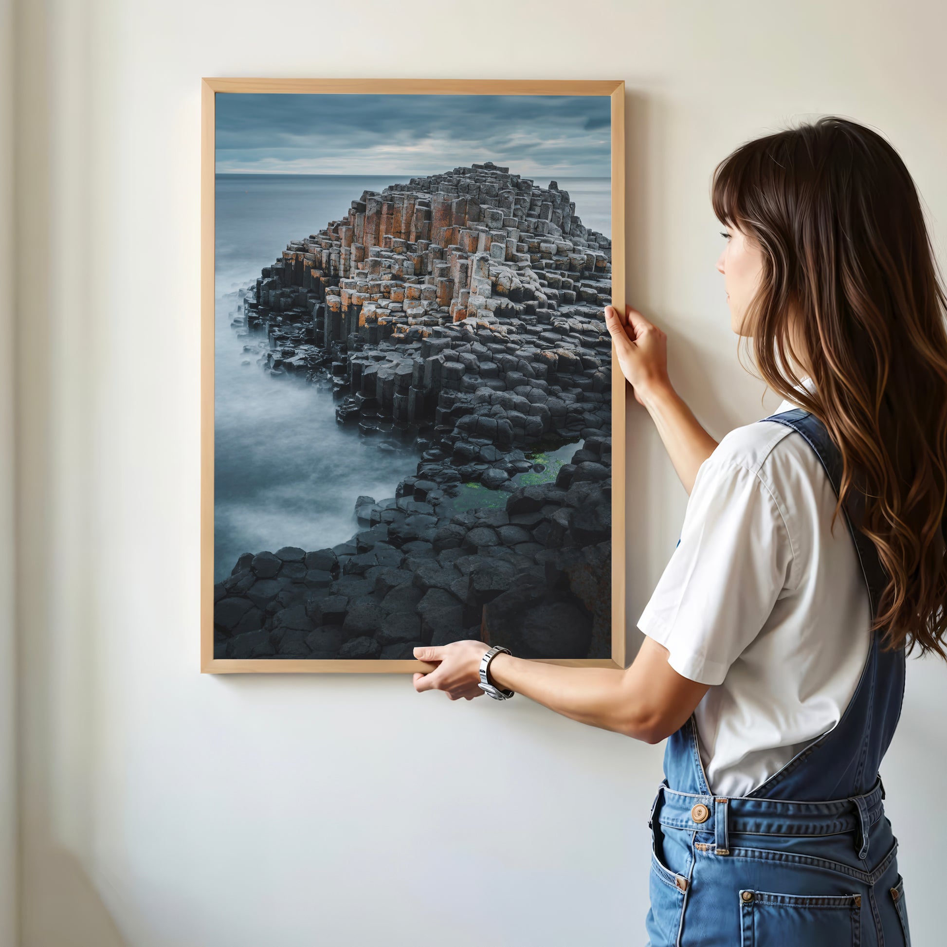 Woman hanging Giant's Causeway framed wall print in minimalist room