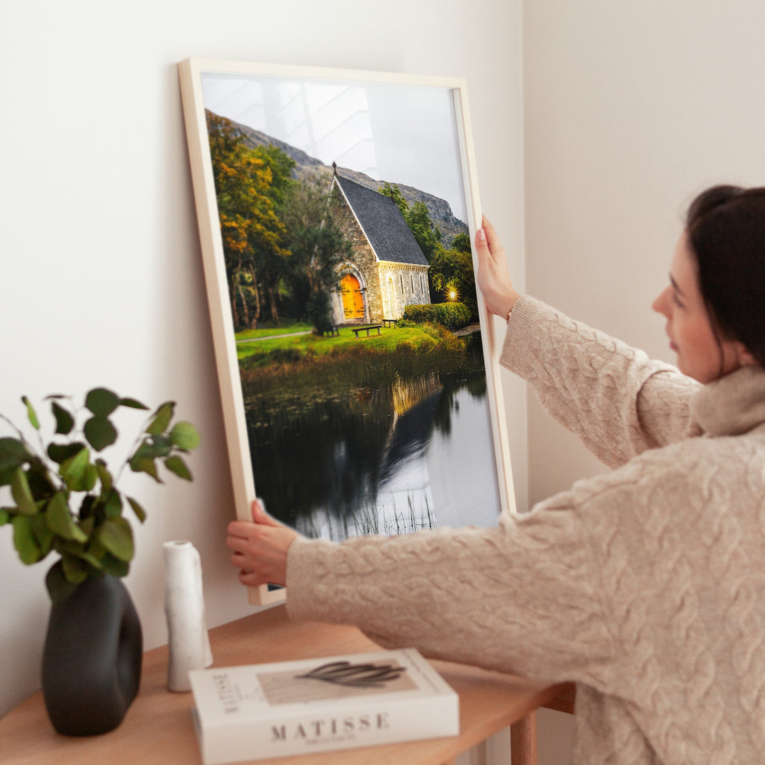 Woman adjusting Irish landscape print of Gougane Barra on wooden table