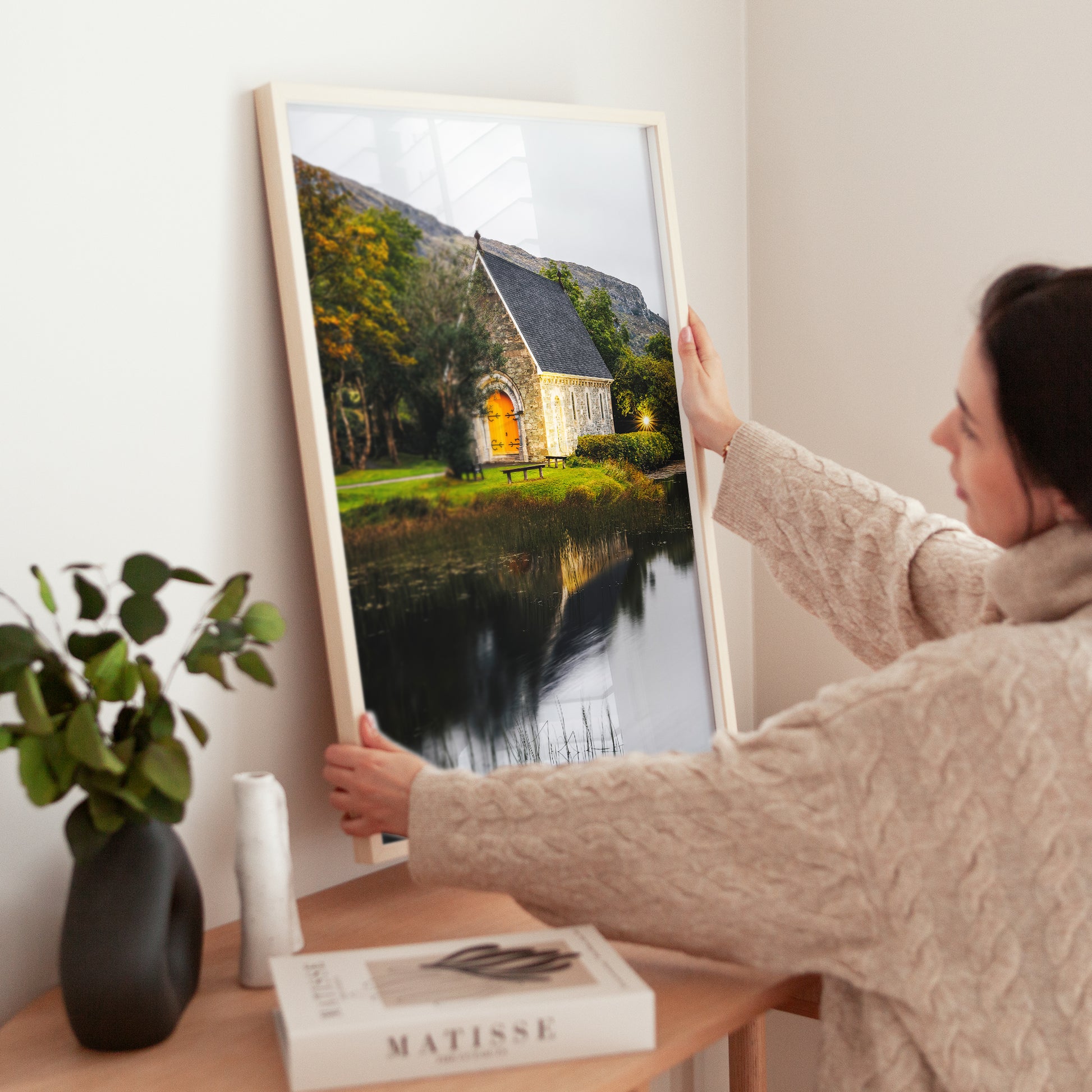 Woman adjusting Irish landscape print of Gougane Barra on wooden table