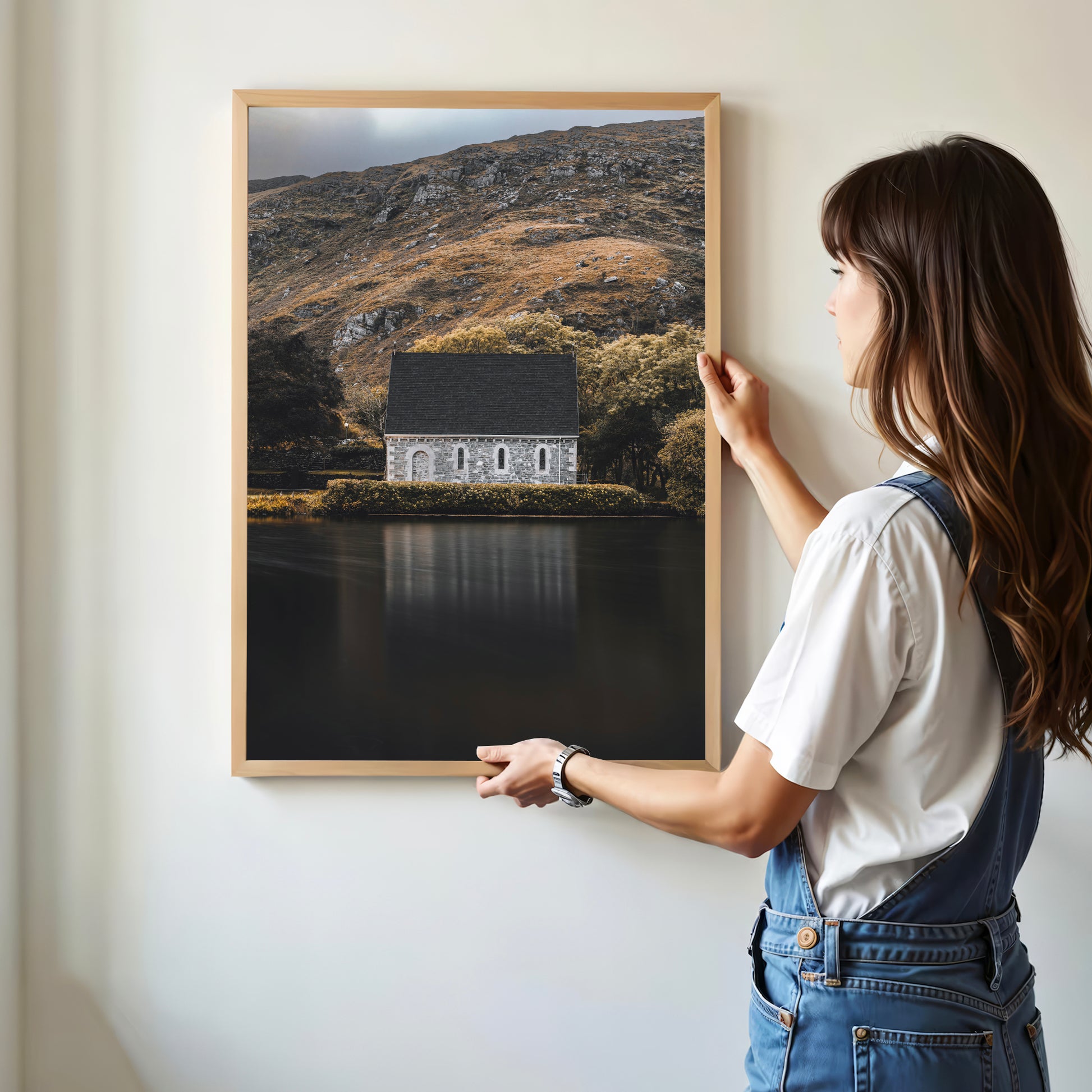 Woman hanging framed Gougane Barra chapel print on wall
