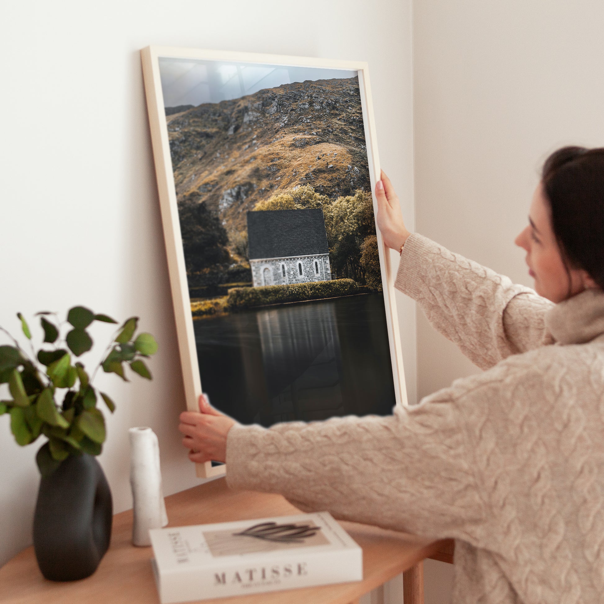 Woman placing framed Irish chapel landscape print on wooden console table