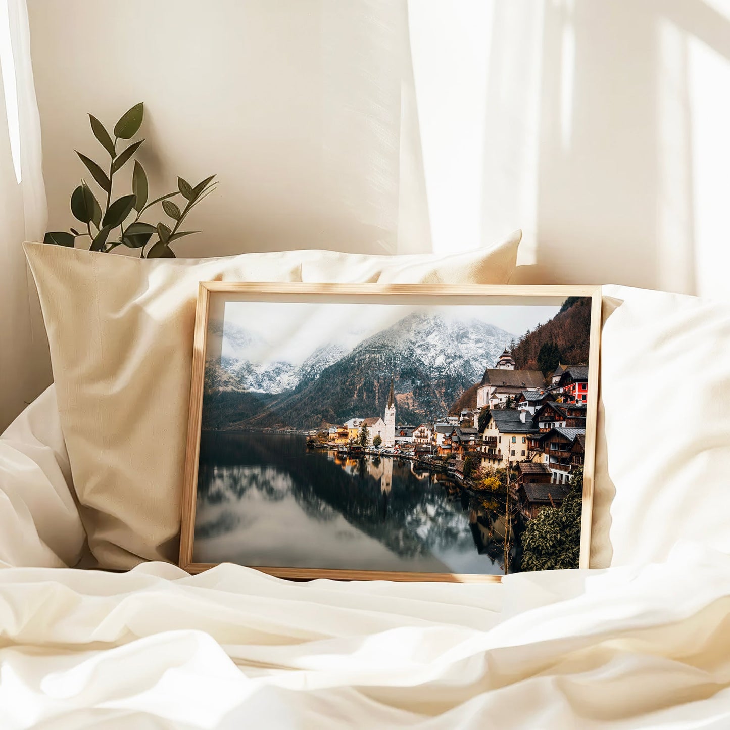 Framed Hallstatt print on a bed with cream cushions and soft sunlight.