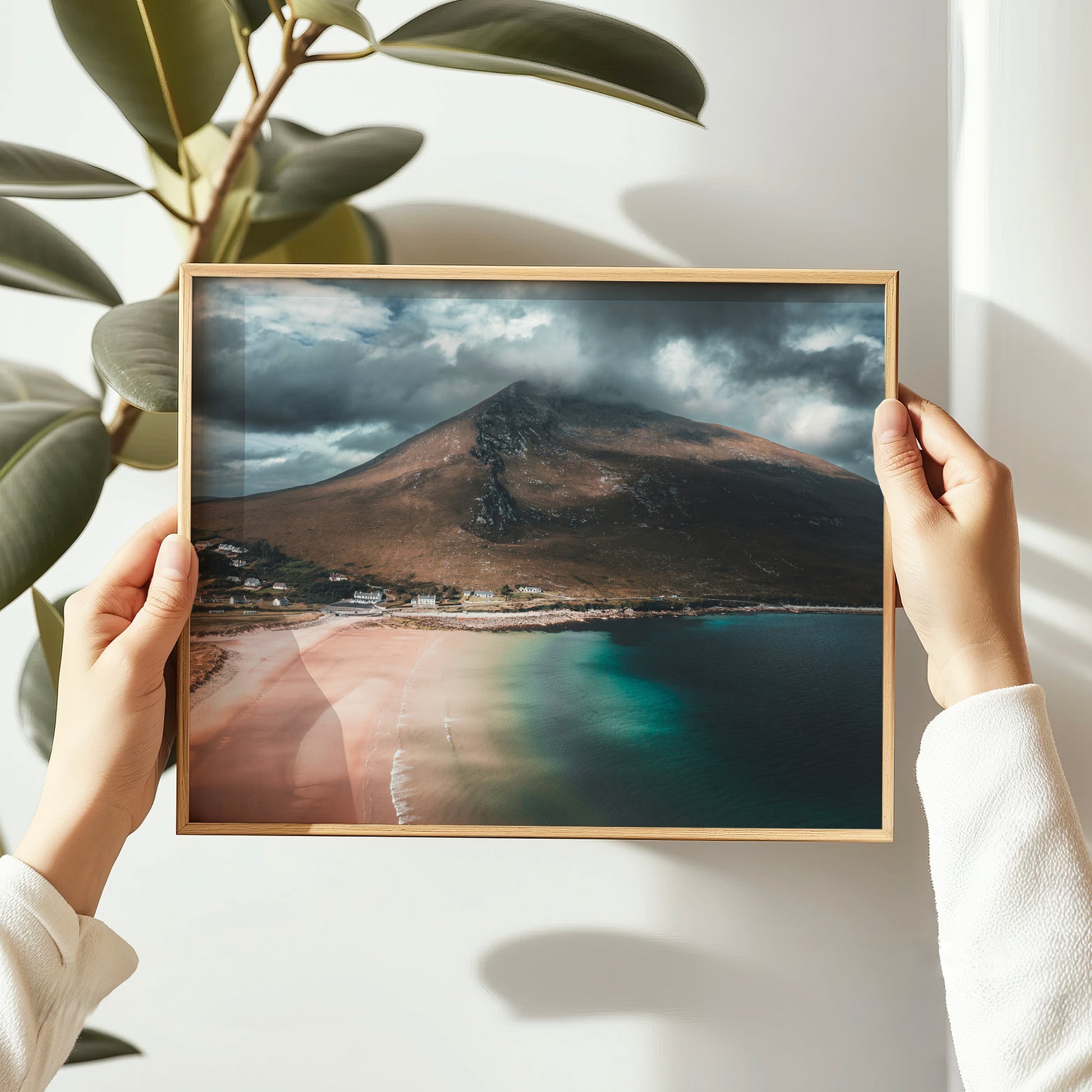 Hands holding a wooden framed Dugort Beach photo print with Irish coastal scenery.
