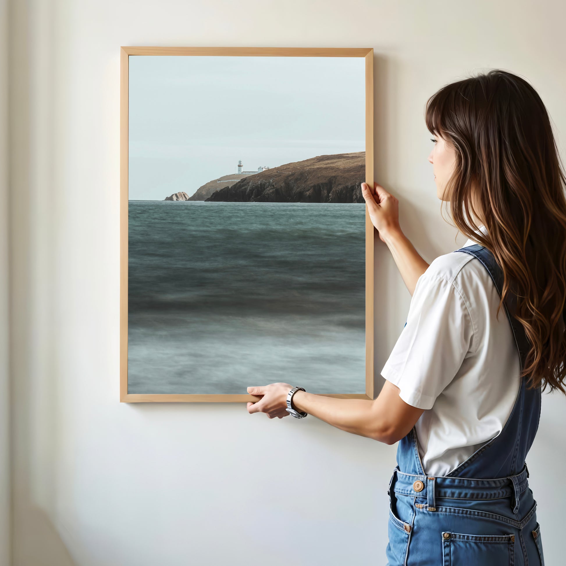 Woman hanging framed Galley Head Lighthouse wall art in modern interior