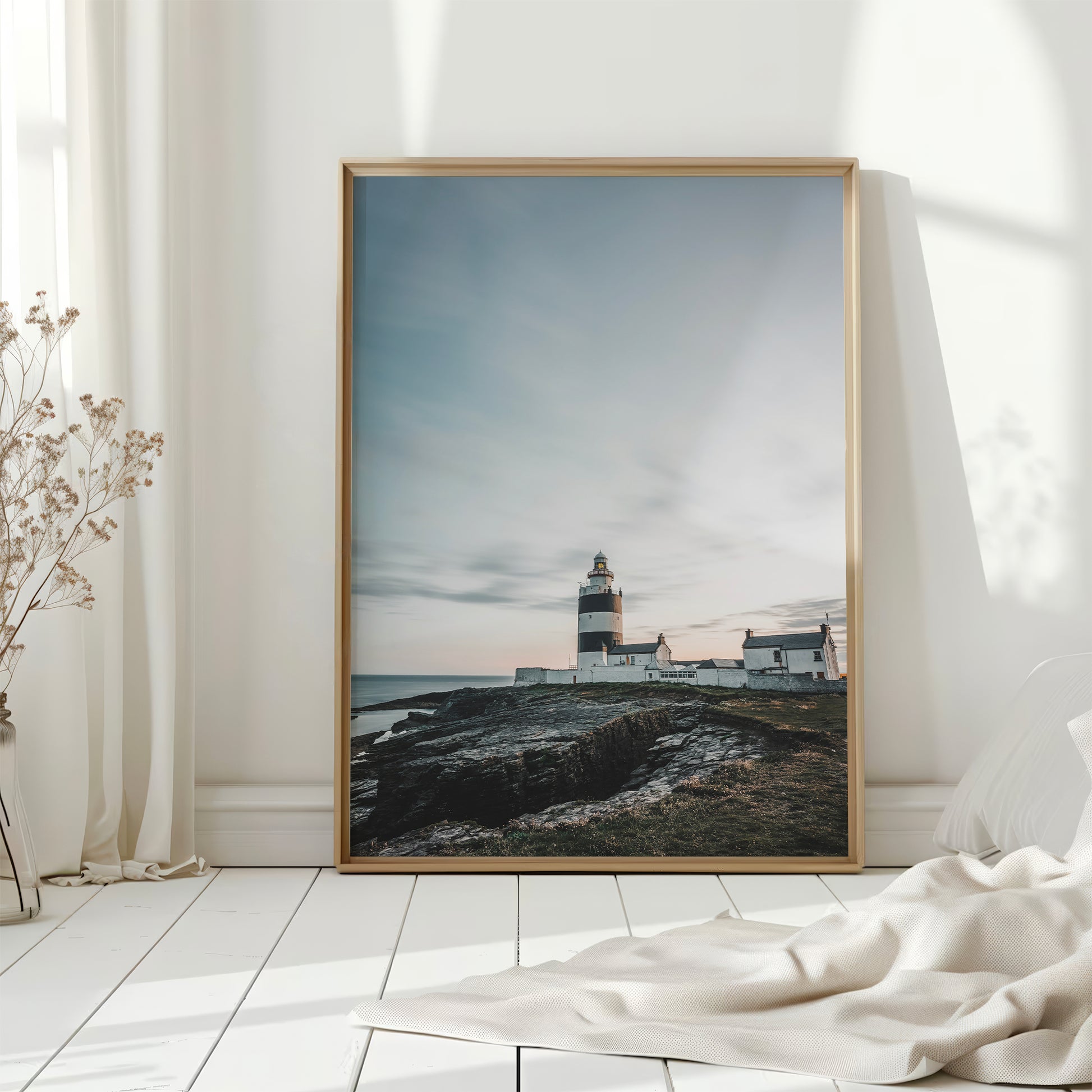 Lighthouse wall print in bright sunlit room with white curtains and dried flowers