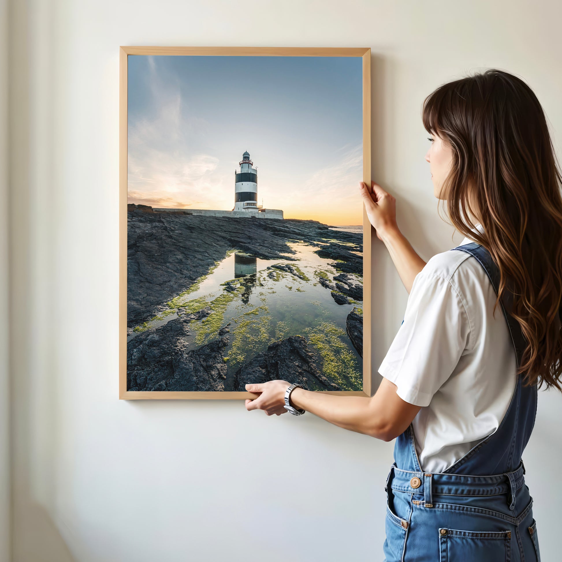 Woman hanging a framed print of Hook Head Lighthouse at golden hour, wall art inspiration