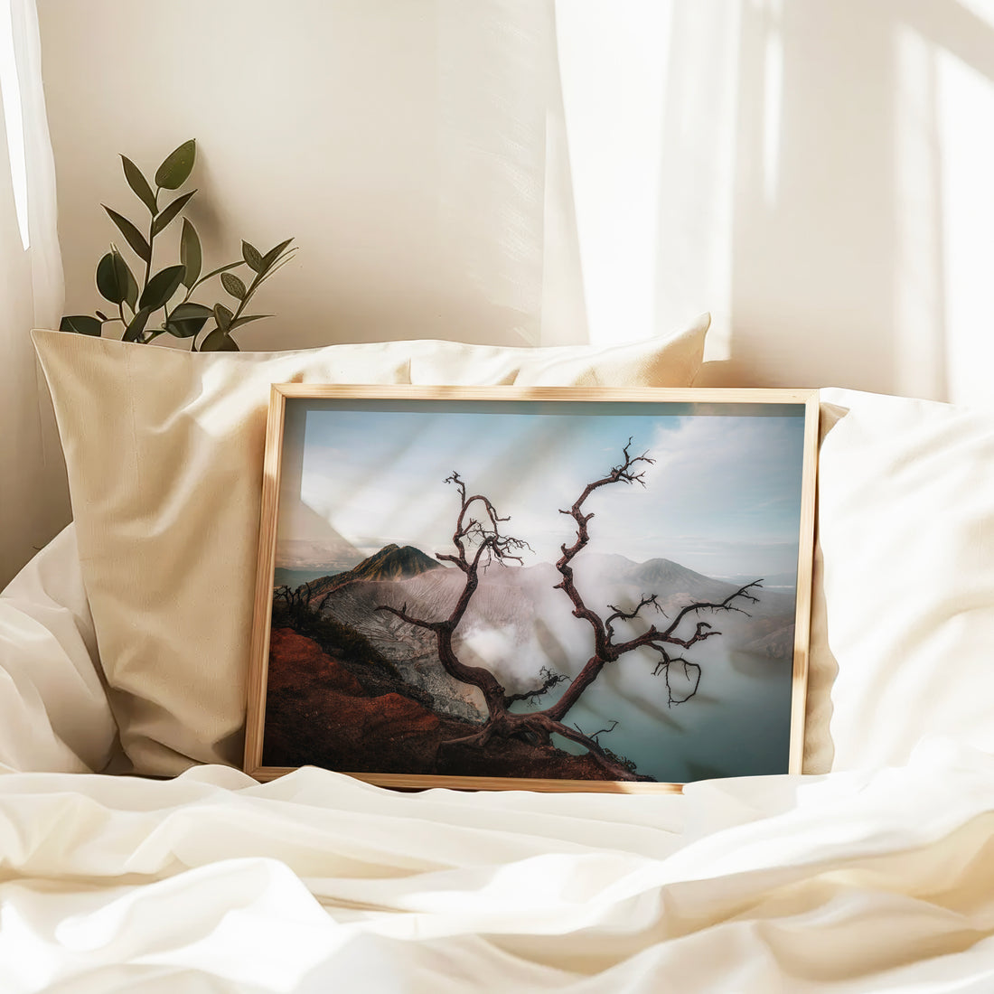 Ijen volcano dead tree framing turquoise crater lake framed print in natural wood frame leaning against pillow on white bed