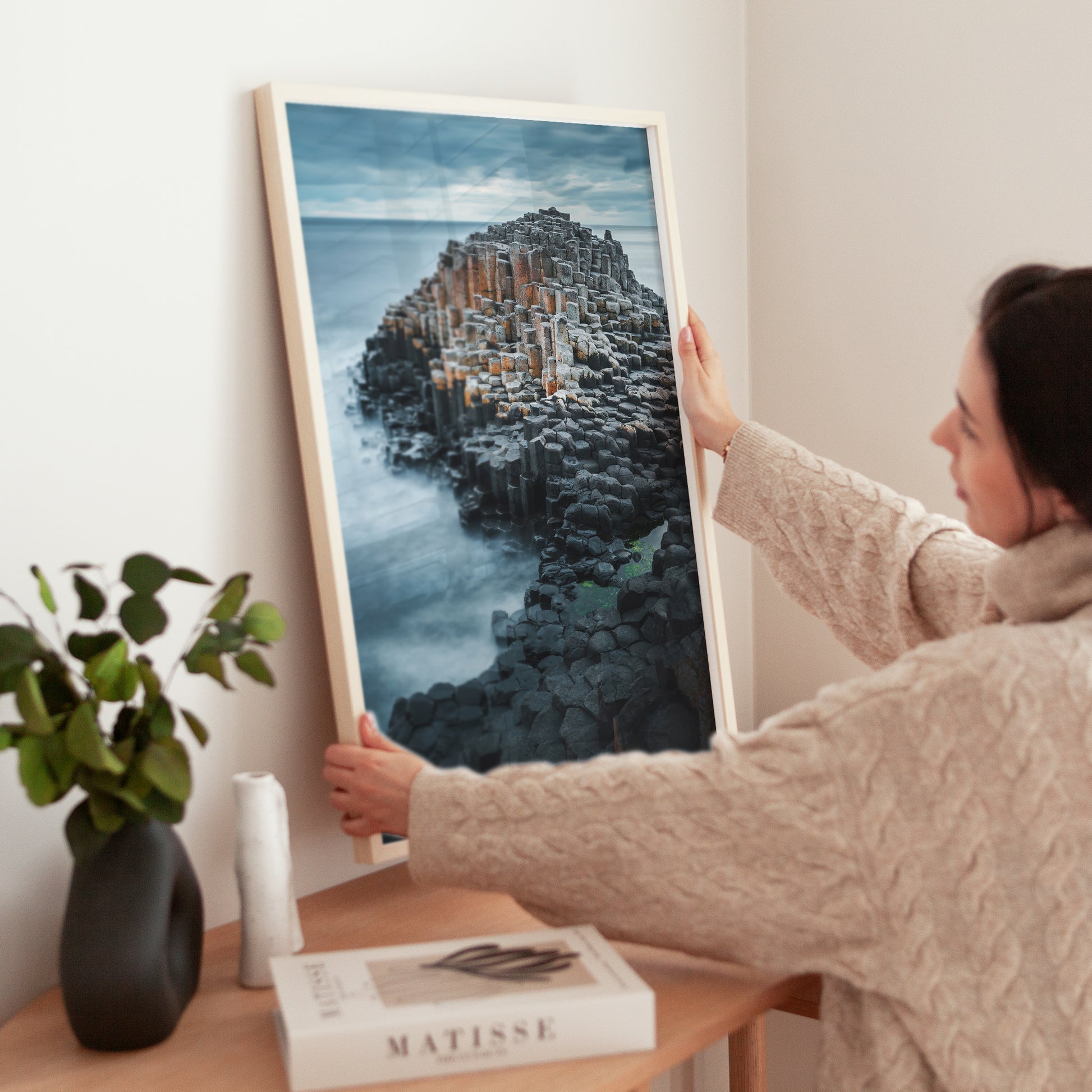 Woman positioning a Giant's Causeway photograph on sideboard in modern home