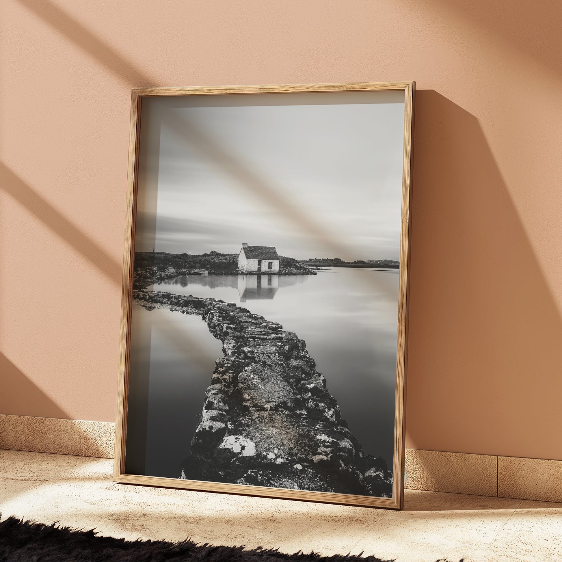 Black and white photo of a Galway bothy leaning against a soft orange wall.