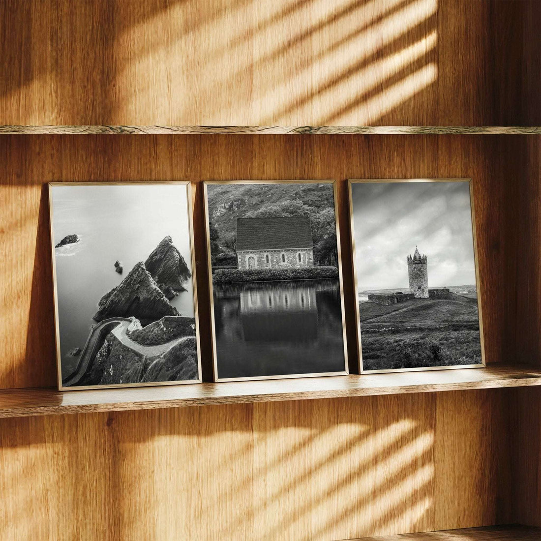 Three black and white Irish landscape prints in wooden frames displayed on a wooden shelf in warm natural light.
