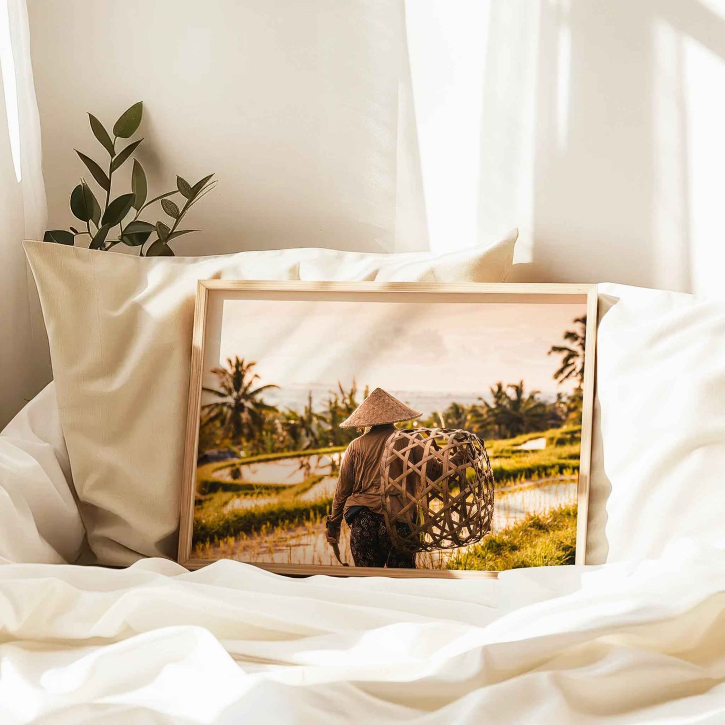 Natural wood framed Jatiluwih Rice Terraces Bali farmer print leaning against pillows in a bedroom setting