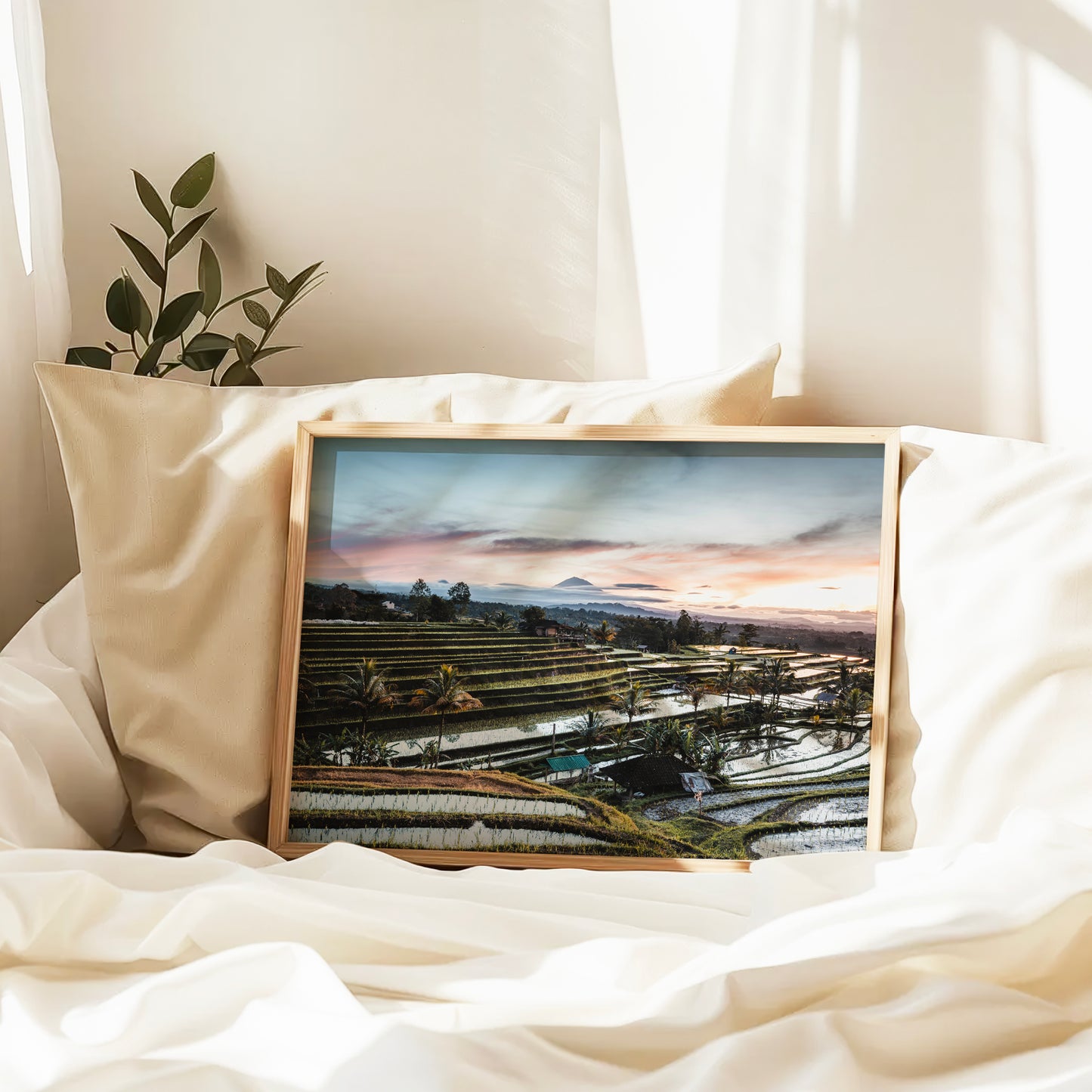 Natural wood framed Jatiluwih Rice Terraces sunrise print Bali Indonesia leaning against pillows in a bedroom setting