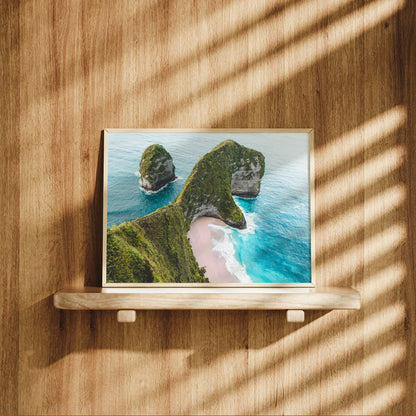 Natural wood framed Kelingking Beach Nusa Penida Bali aerial print displayed on a wooden shelf