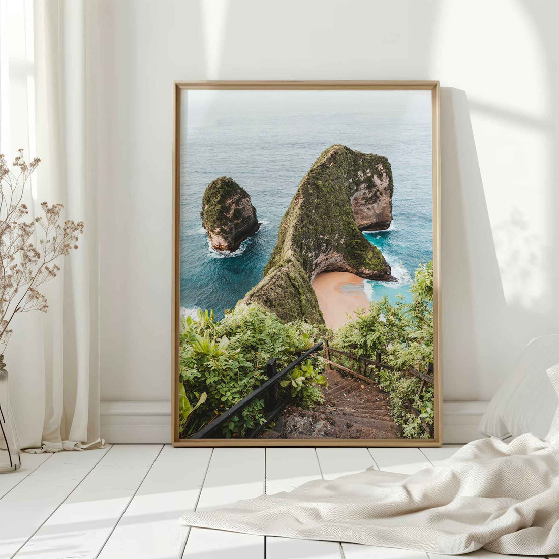 Kelingking Beach Nusa Penida large framed wall art print in natural wood frame leaning against white wall with dried flowers