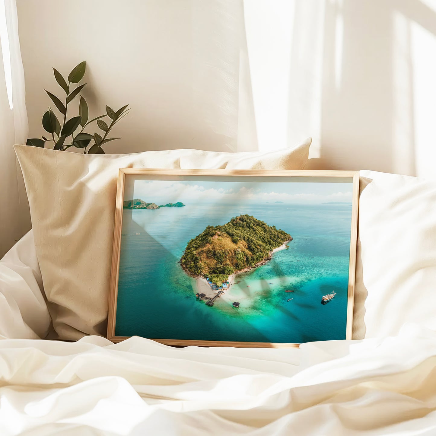 Natural wood framed Kelor Island Komodo aerial print leaning against pillows in a bedroom setting