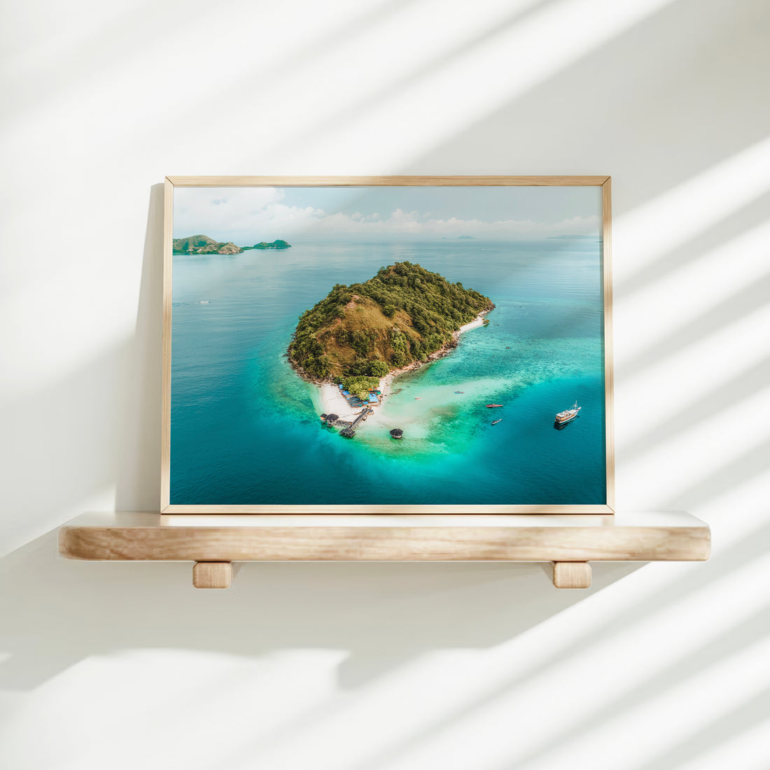 Gold framed aerial print of Kelor Island Komodo on a minimalist wall shelf with soft natural light