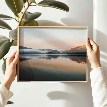 Hands holding framed Lake Manapouri New Zealand photography print in natural oak frame beside indoor plant
