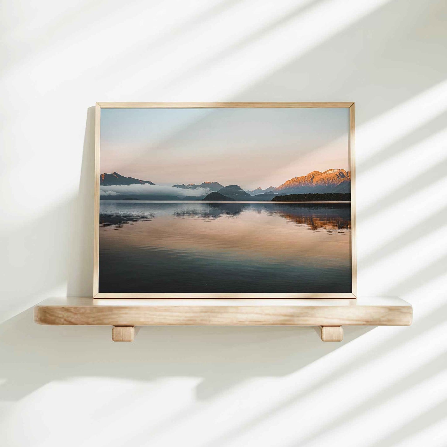 Lake Manapouri New Zealand landscape photography print in natural wood frame on floating shelf against white wall with light shadows