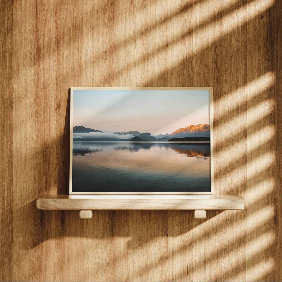 Framed Lake Manapouri New Zealand landscape print in natural wood frame leaning on shelf against warm oak panelled wall