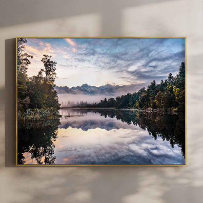 Framed Lake Matheson reflection sunrise photography print in gold float frame mounted on warm beige wall with window light shadows