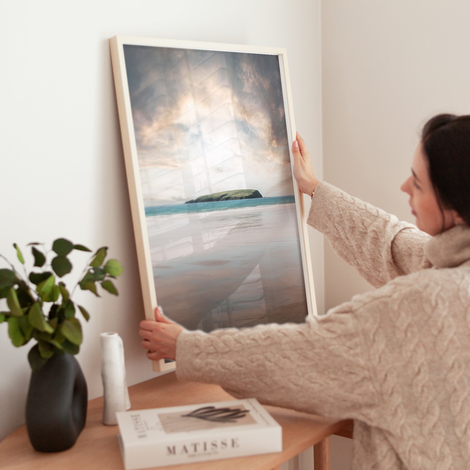 Woman placing Keel Beach print on sideboard with natural decor in a cosy interior