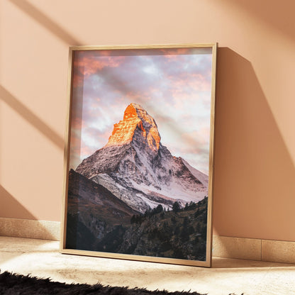 Rustic oak-framed artwork of the Matterhorn illuminated by alpenglow, against soft peach walls.