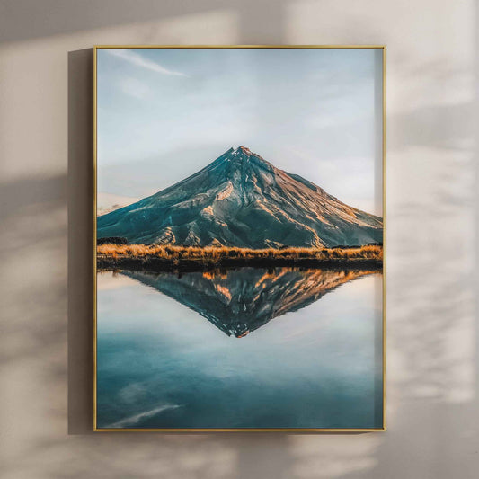Framed Mount Taranaki reflection photography print in gold float frame mounted on warm beige wall with window light shadows