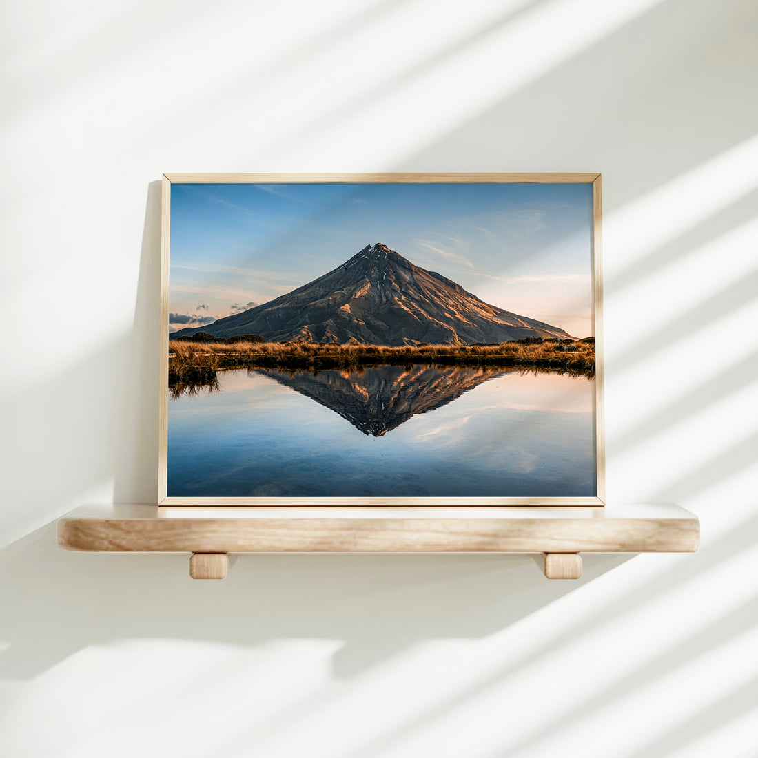 Mount Taranaki volcano reflection tarn landscape photography print in natural wood frame on floating shelf against white wall with light shadows