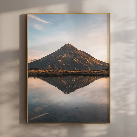 Framed Mount Taranaki sunset reflection photography print in gold float frame mounted on warm beige wall with window light shadows