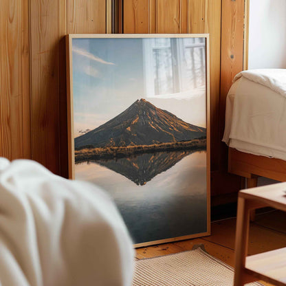 Framed Mount Taranaki sunset reflection print in natural wood frame leaning against pine panelled bedroom wall