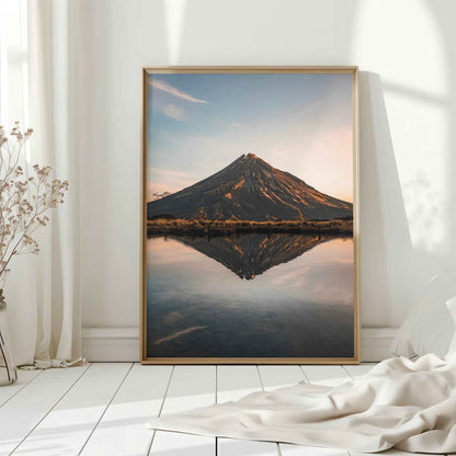 Natural wood framed Mount Taranaki sunset reflection print leaning against white wall on white floorboards in minimal Scandinavian interior
