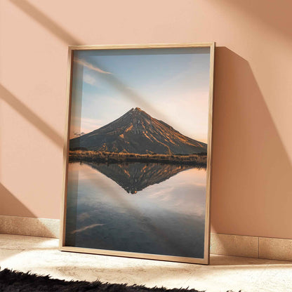 Framed Mount Taranaki sunset reflection print in light wood frame leaning against terracotta wall with dramatic shadows