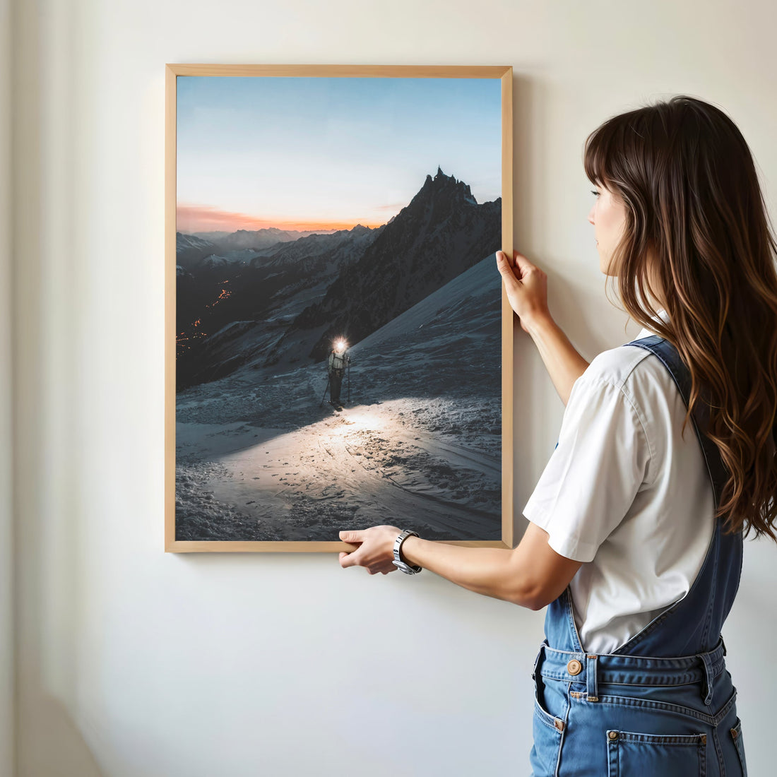 Woman hanging a framed alpine glacier print of a mountaineer at twilight