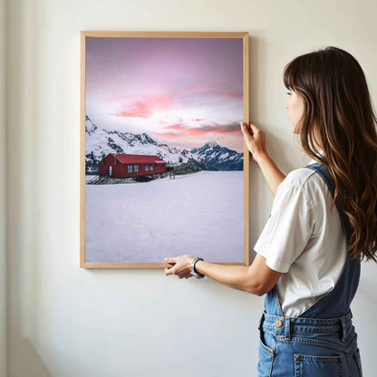 Woman hanging framed Mueller Hut and Mount Cook winter photography print in natural oak frame on white wall