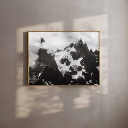 Framed black-and-white photograph of the Needles of Chamonix with dramatic clouds, mounted on a beige wall with natural light shadows.