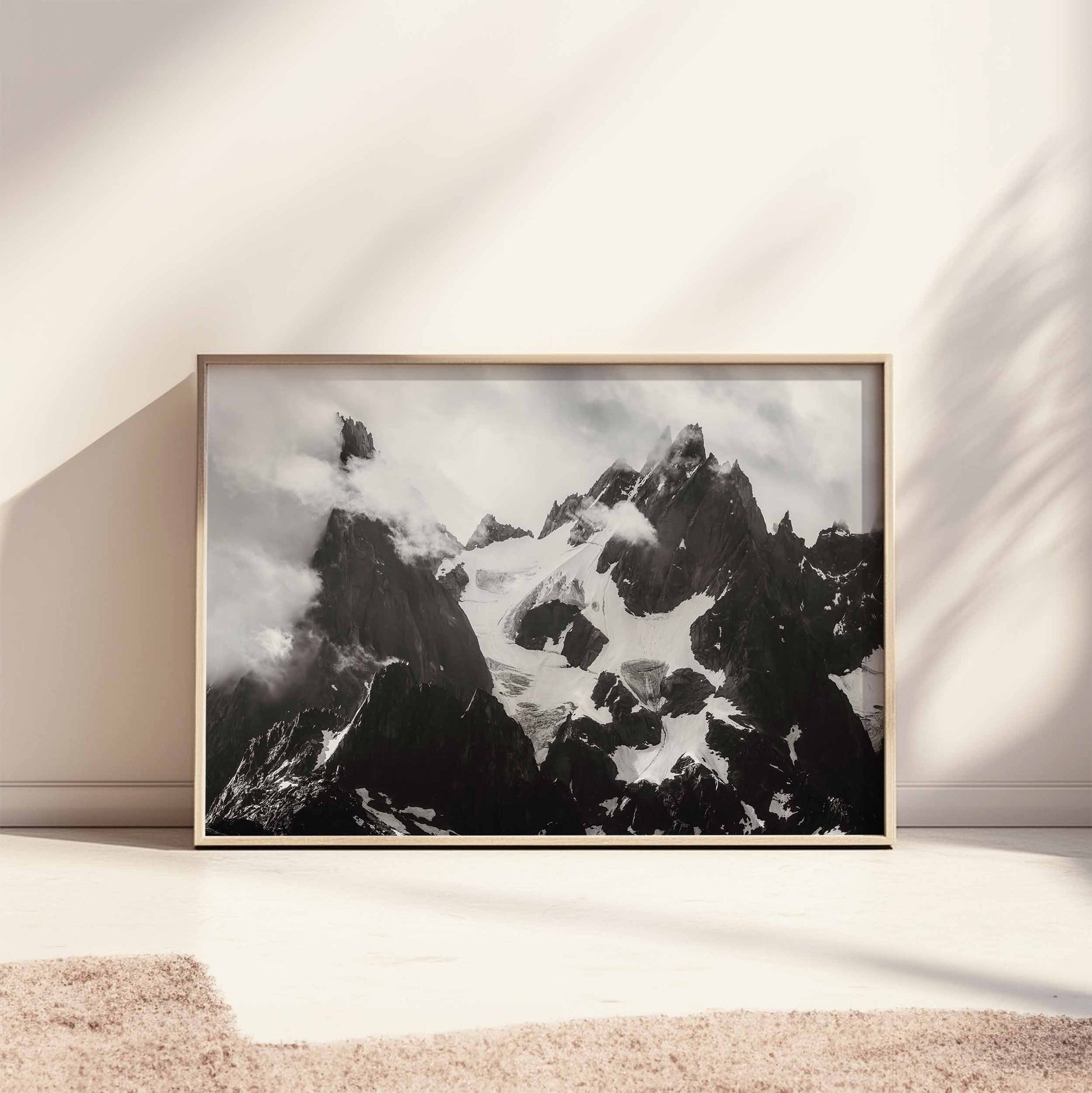 Large framed black-and-white print of the Needles of Chamonix leaning against a cream-colored wall with soft lighting.