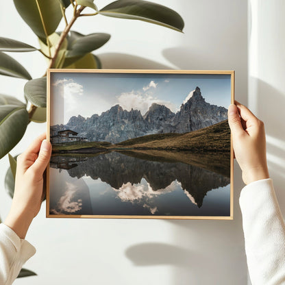 Hands holding framed Passo Rolle reflection print with pale sky and mountain peaks
