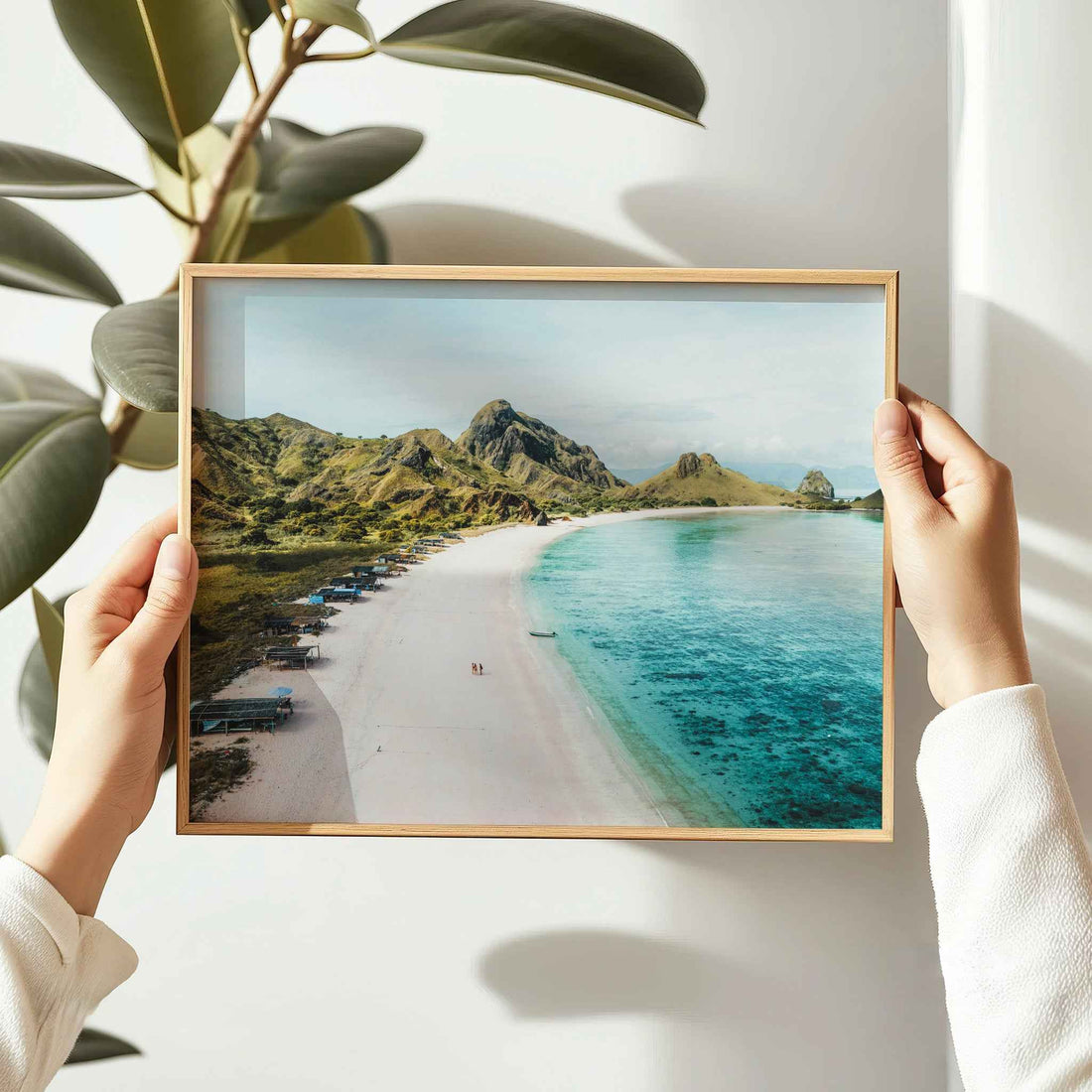 Hands holding Pink Beach Padar Island Komodo National Park framed wall art print in natural oak wood frame against white wall