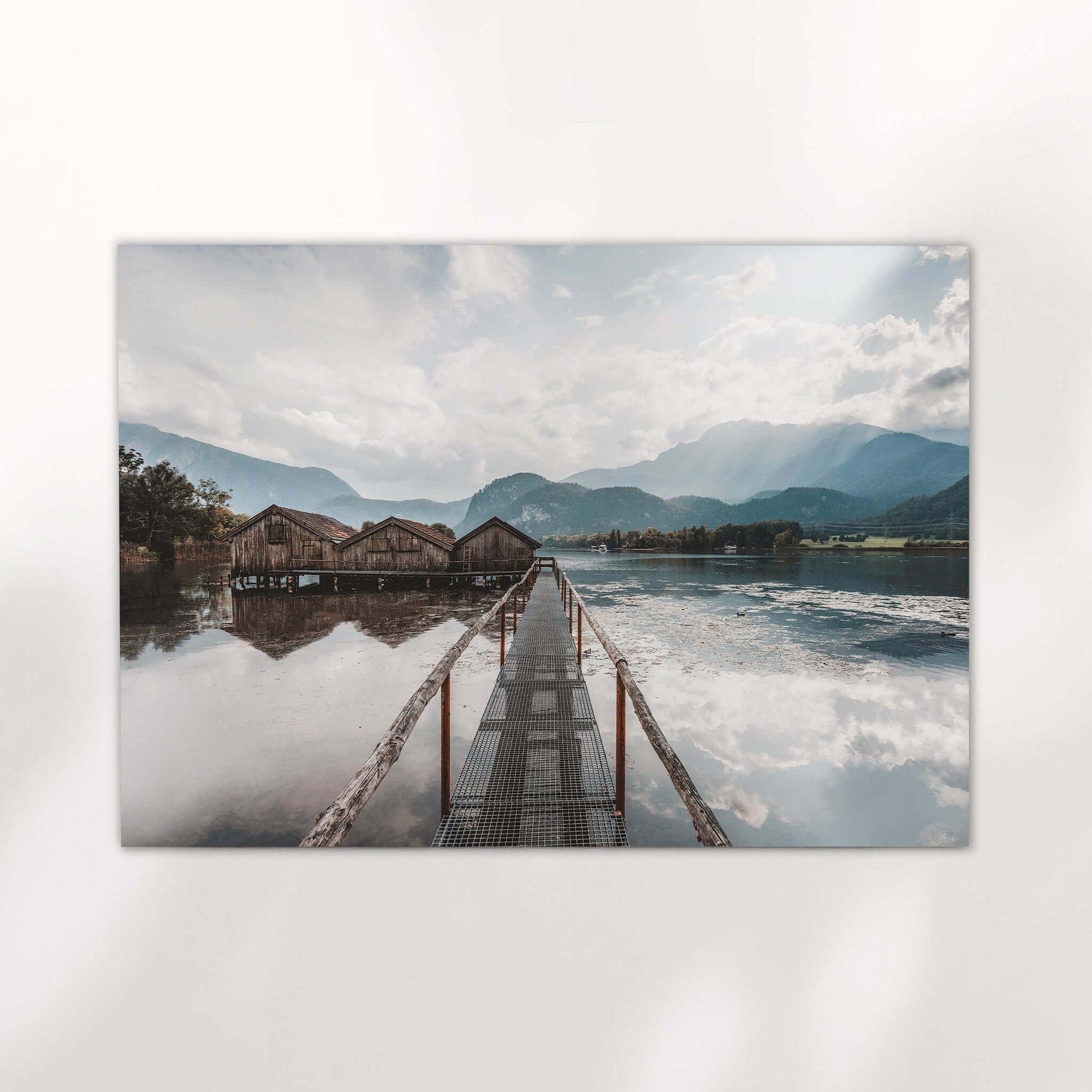 Sunrise light over calm Kochelsee water with alpine peaks and boathouses