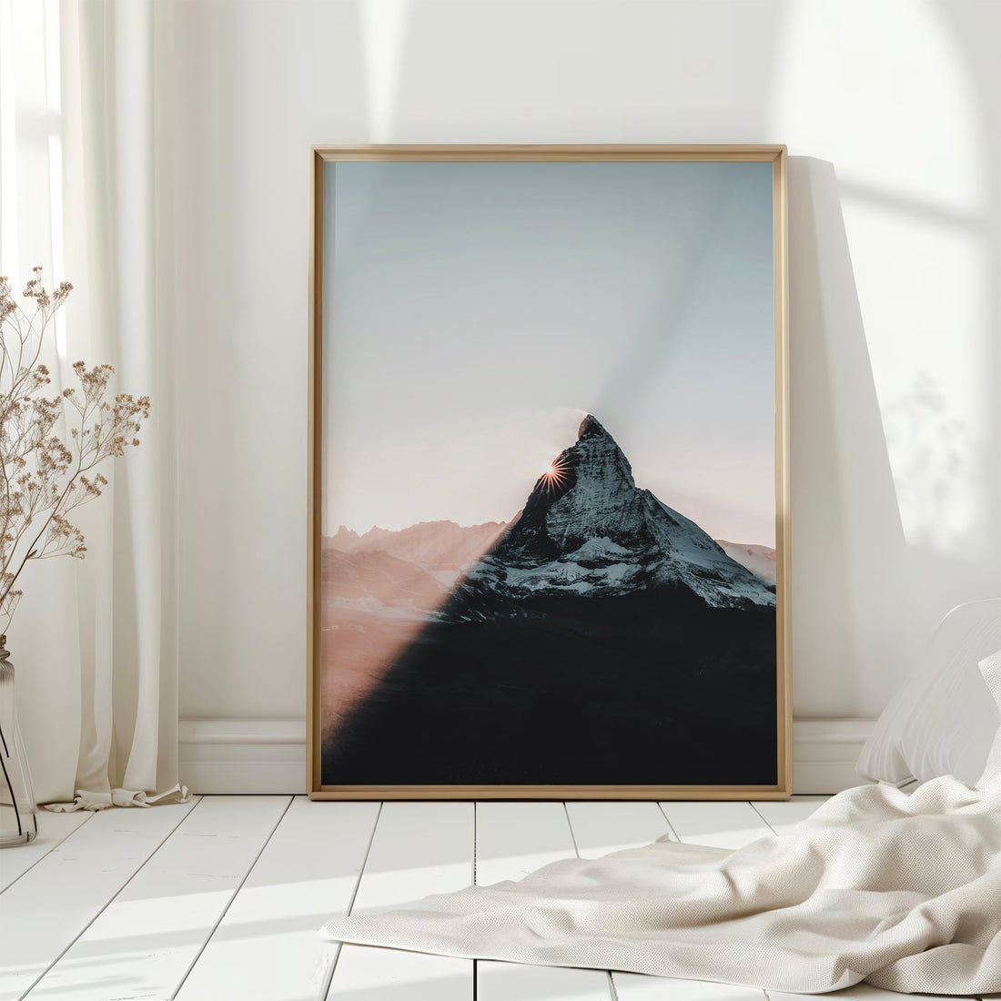 Framed Matterhorn print with sunset hues on floor by white curtains