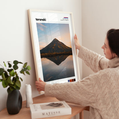 Hands adjusting a framed Mount Taranaki landscape wall art print in a calm living space