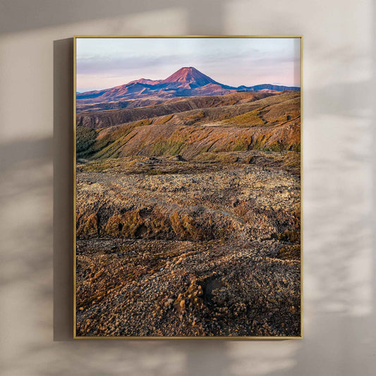 Framed volcanic landscape photography print in gold float frame mounted on warm beige wall with window light shadows